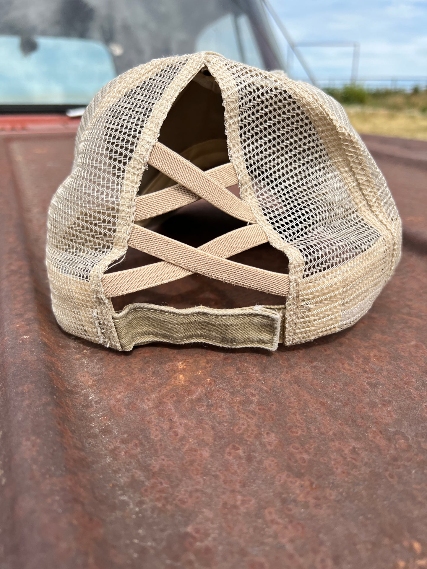 Back of distressed Khaki baseball cap with stretchy criss cross straps and velcro adjustabale strap.