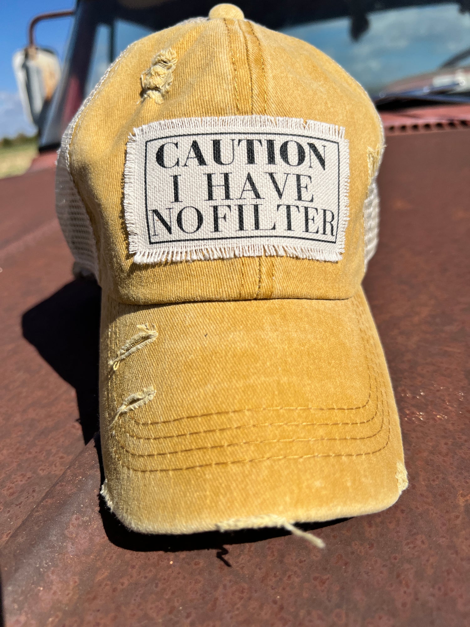 Material Patch with saying "Caution I Have No Filter"  on distressed mustard baseball cap 