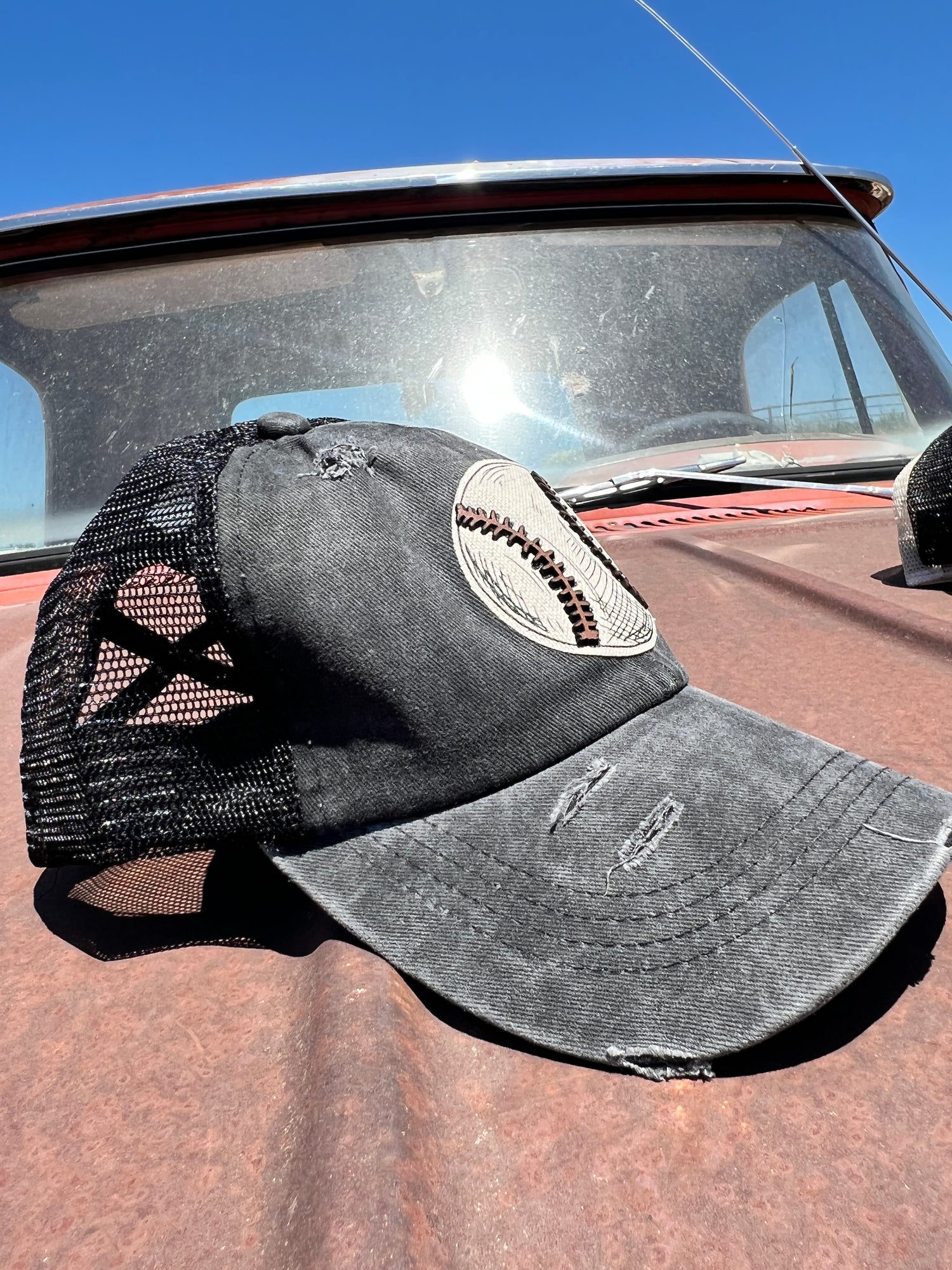 Side profile of black distressed baseball cap. Light distressing on bill and black mesh 