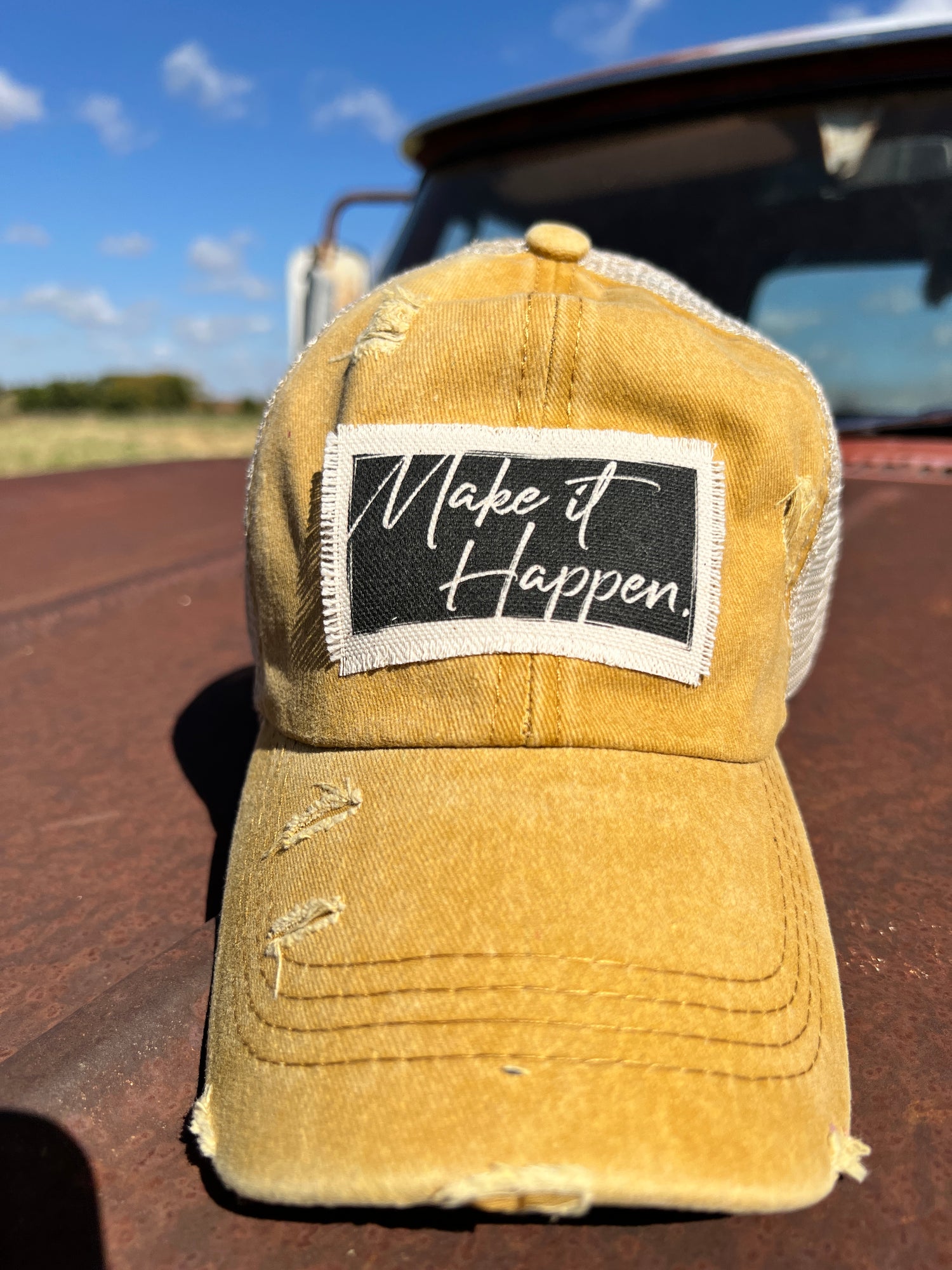 Distressed Mustard baseball cap with material patch with saying "Make it Happen" with black backround. 
